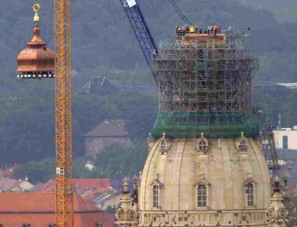 Celtnis paceļ vara kupolu un zelta krustu uz rekonstruētās Frauenkirche virsotnes Drēzdenē, Vācijā